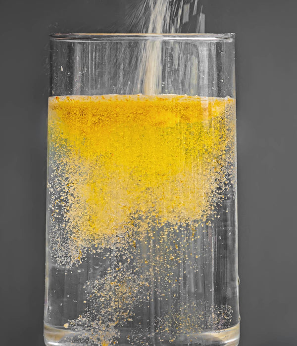 MULTIMIX FX - SUPLEMENTO ALIMENTICIO. Vaso con agua al cual se le está vertiendo el polvo/producto. El liquido se torna de un color naranja.