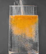 ZINOVID C3 (POLVO) - SUPLEMENTO ALIMENTICIO. Vaso de cristal con agua al que se le agrega el polvo/producto, mientras el agua cambia de color a naranja al contacto con el ingrediente. 
